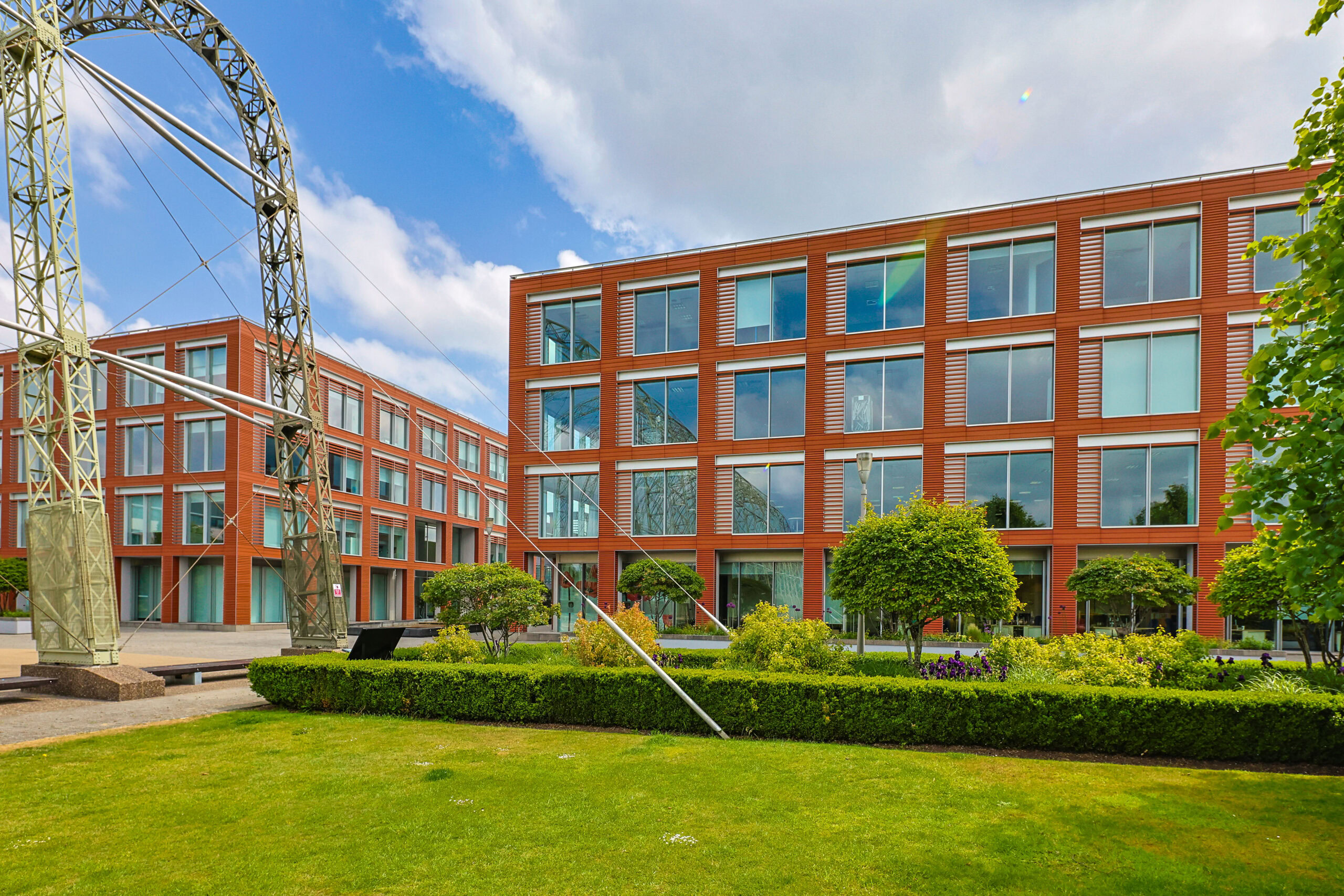 Modern red-brick office buildings with large windows and green landscaping under a partly cloudy sky.