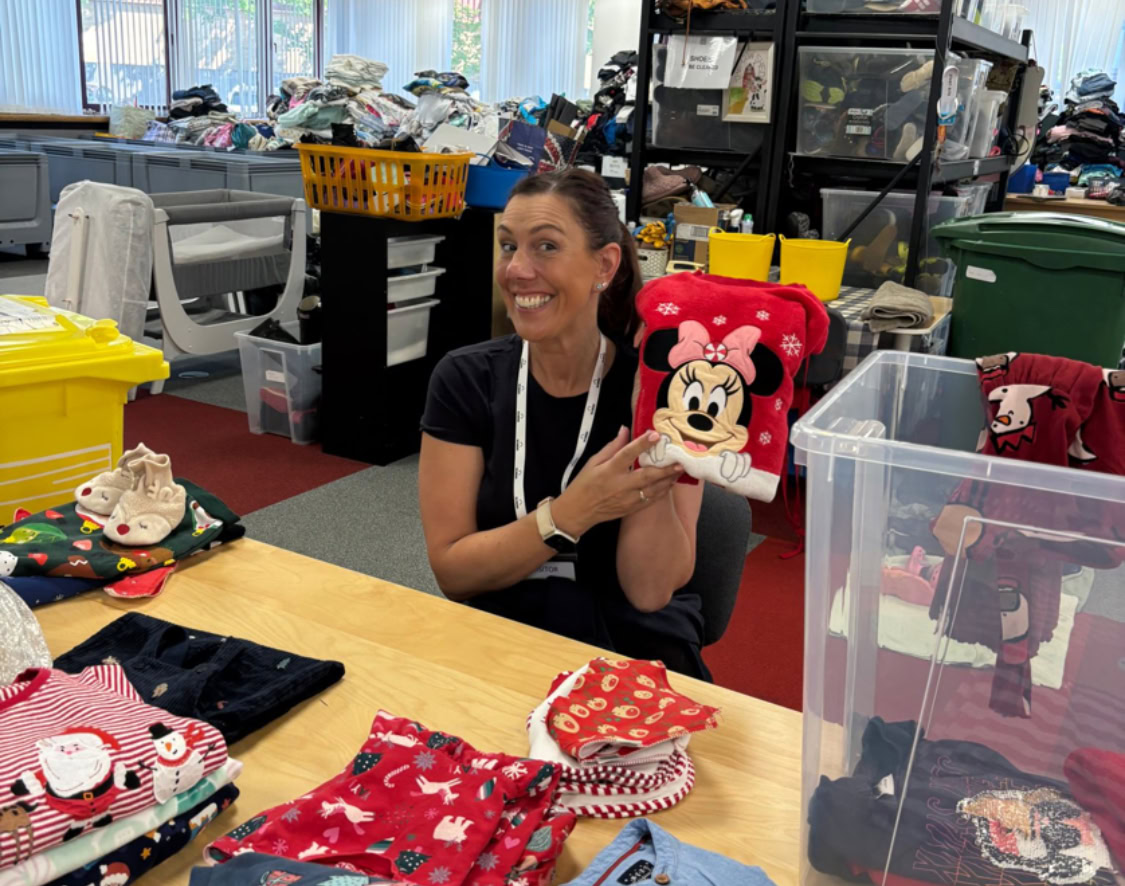 A woman sits at a table sorting and holding up a folded red Minnie Mouse toddler outfit.