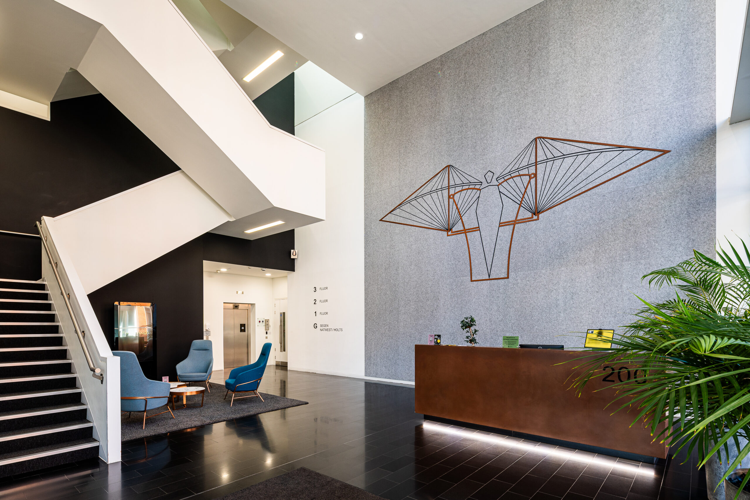 Modern office lobby with staircase, seating area, wall art, and reception desk.
