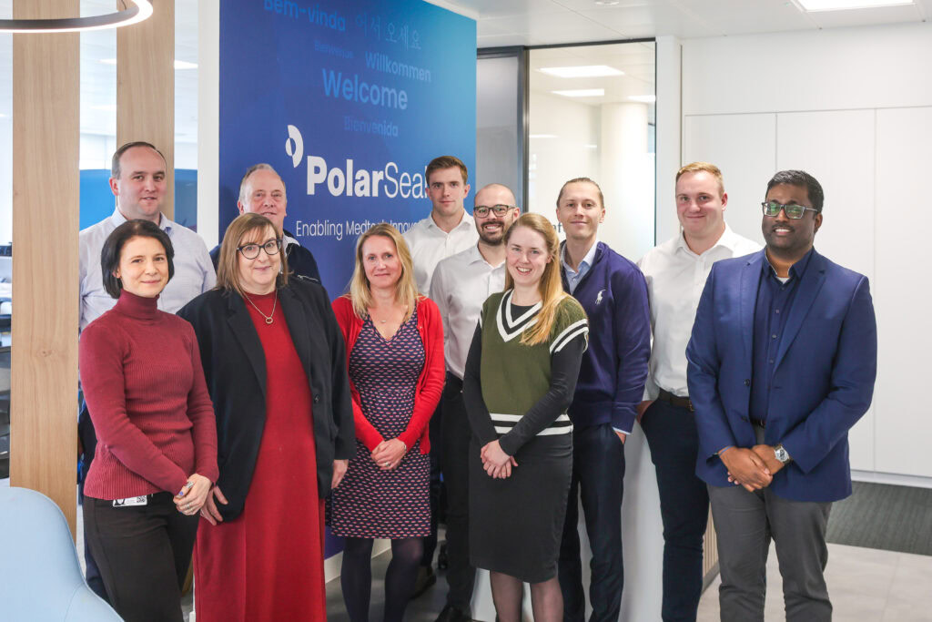 A group of eleven people pose for a photo in an office next to a PolarSeal welcome sign.