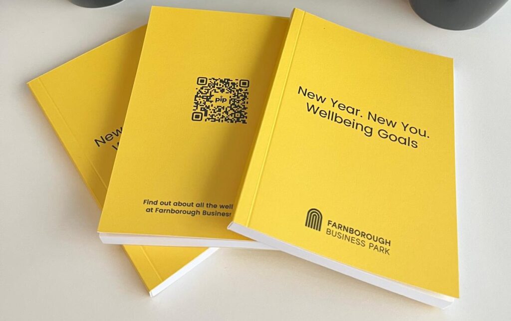 Rows of black mugs and bright yellow wellbeing goal booklets branded with Farnborough Business Park.