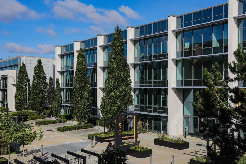 Modern office building with large glass windows, tall trees, and a sign displaying the number 150.